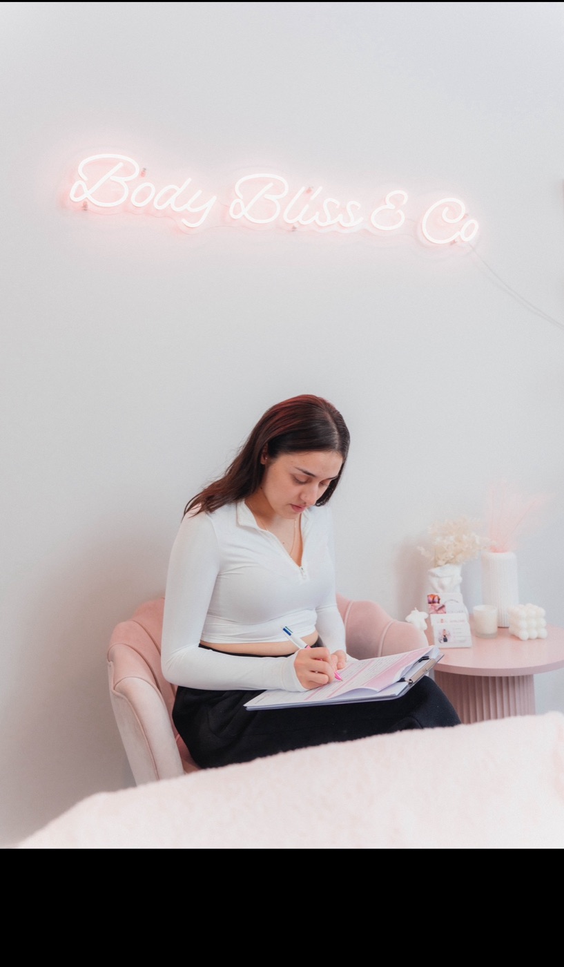 Studio wall with the Body Bliss & Co neon sign above the founder writing client notes